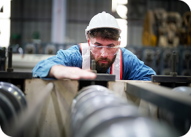 À l'intérieur d'une usine, un ouvrier industriel en action sur une presse à métaux tenant une pièce d'acier prête à être travaillée.