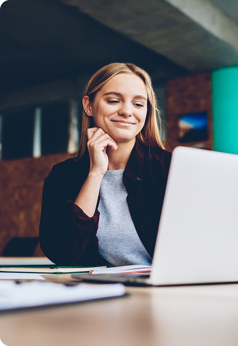 Une graphiste à succès regarde un tutoriel sur des idées créatives sur un ordinateur portable pendant le processus de travail au bureau. Une étudiante positive aux cheveux blonds lit les actualités commerciales sur un netbook