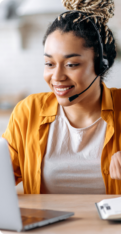 Jeune femme afro-américaine sympathique et attirante portant un casque, employée d'un centre d'appels, opératrice de support, travaillant sur un ordinateur portable, effectue une consultation en ligne avec un client, regardant l'écran, souriant