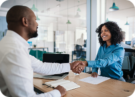 Un manager afro-américain souriant assis à son bureau dans un bureau serrant la main d'un candidat à un emploi après un entretien