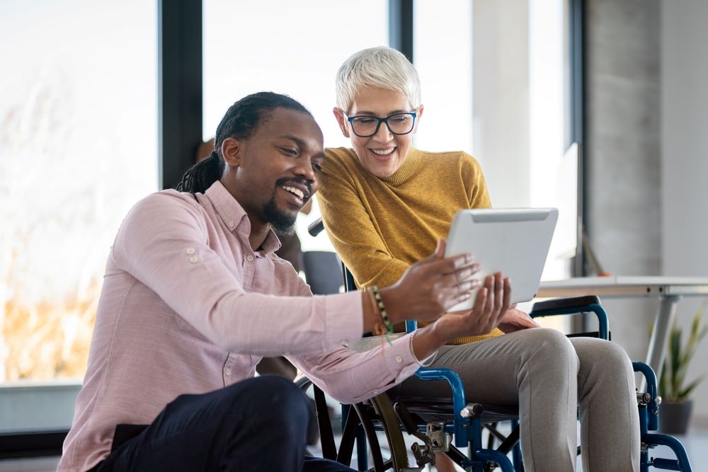 Femme d'affaires en fauteuil roulant travaillant avec un collègue dans un bureau moderne et inclusif. Diversité, assistance