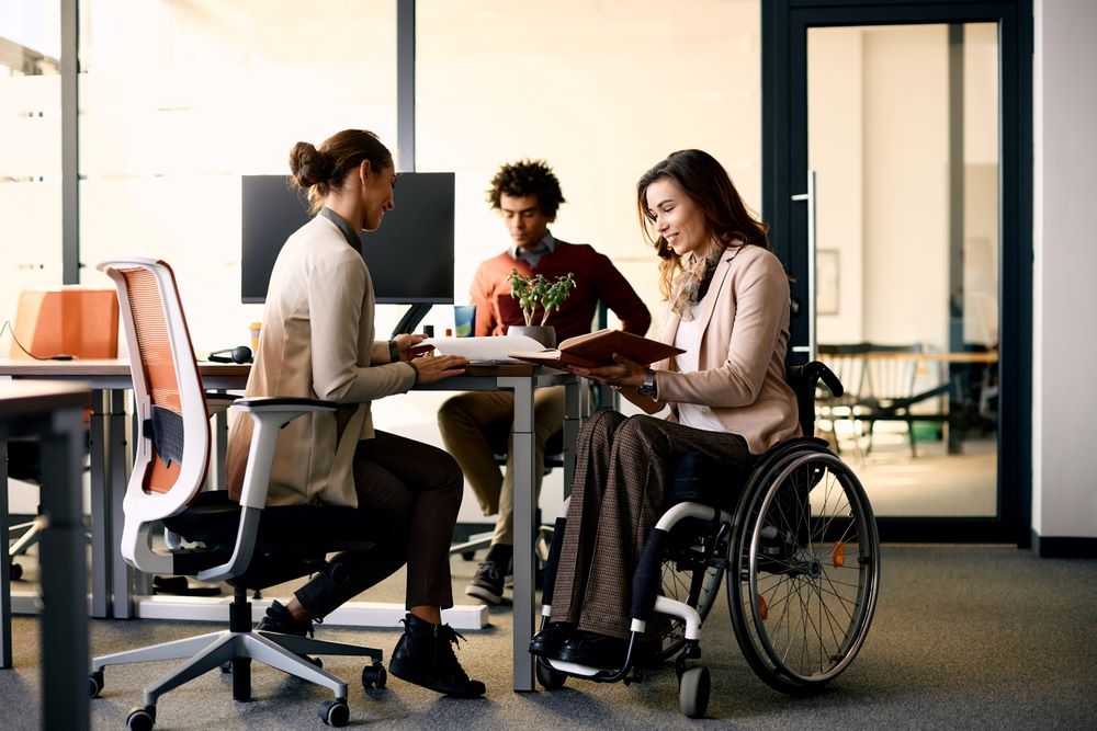 Une femme d'affaires heureuse avec un handicap et une collègue de sexe féminin coopérant dans le cadre de la paperasserie au bureau.
