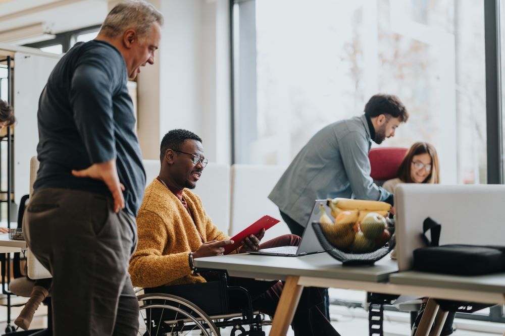 Un environnement de bureau moderne et inclusif avec une équipe diversifiée collaborant. Une personne en fauteuil roulant s'engage activement avec ses collègues.